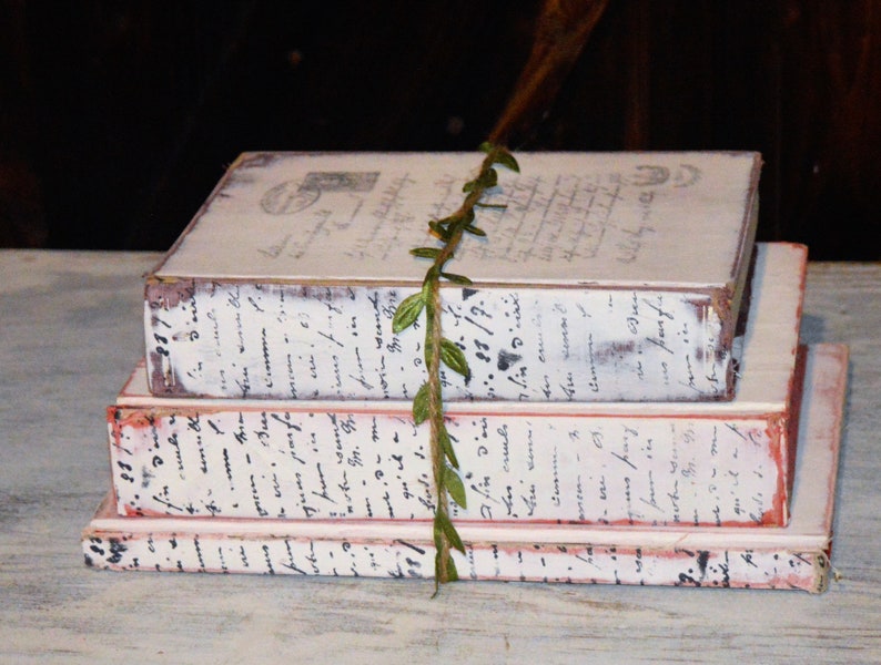 Pode incluir: Uma pilha de tr&ecirc;s livros de estilo vintage com capas pintadas de branco e escrita preta. Os livros s&atilde;o decorados com uma videira verde com folhas.