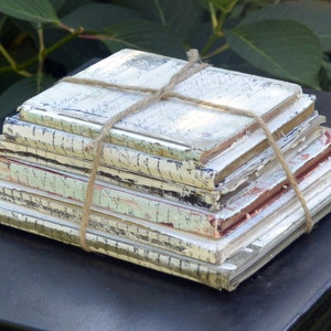 May include: A stack of vintage, worn, and aged books tied together with twine. The books have a cream-colored paper cover with black lettering and are stacked on a black surface.