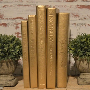 May include: Six gold-painted books with different titles, including "Gap Creek", "KINGSBURY", "BETWEEN SUNDA", "the teacher who couldn't read", "ATHOLDICKSON RIVER RISING", and "ULTIMATE DOOM".