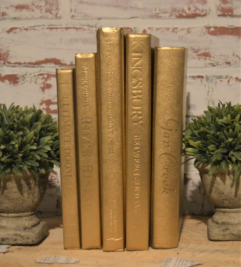 May include: Six gold-painted books with different titles, including "Gap Creek", "KINGSBURY", "BETWEEN SUNDA", "the teacher who couldn't read", "ATHOLDICKSON RIVER RISING", and "ULTIMATE DOOM".