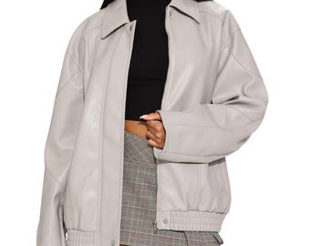 May include: A light gray faux leather jacket featuring a classic collar, long sleeves with cuffs, and a front button closure. The jacket is worn over a black mock neck top and a gray plaid mini skirt, showcasing a structured and layered appearance.