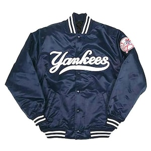 Può includere: Giacca da baseball dei Yankees in raso blu navy con scritte e finiture bianche. La giacca presenta la scritta "Yankees" sul petto e una toppa con il logo della squadra sulla manica. Ha una chiusura con bottoni e polsini a coste.