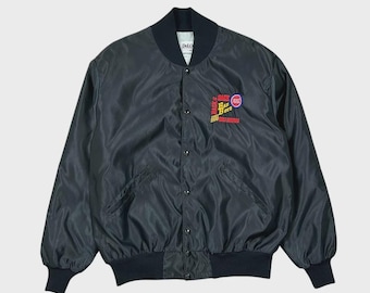 May include: A black bomber jacket with a ribbed collar, cuffs, and hem. The front features a snap-button closure and an embroidered patch on the left chest with the text "BACK 2 BACK BAD BOYS" in red and yellow, alongside a small circular logo.
