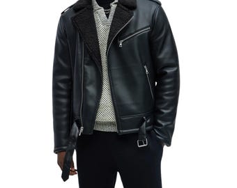 May include: A black faux leather motorcycle jacket featuring a wide black sherpa collar, an asymmetrical silver zipper closure, and a buckled belt at the hem. The jacket includes silver zippered pockets on the chest and sides, worn over a textured sweater.