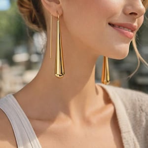 May include: Gold-coloured, elongated teardrop earrings. The earrings are suspended from a thin, straight gold wire. The design is simple and elegant, with a polished finish. The earrings are a statement piece.