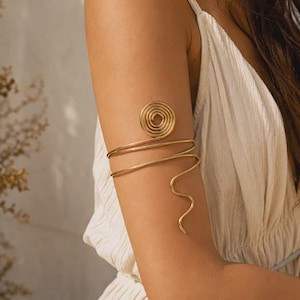 May include: A gold-toned metal arm cuff featuring a circular spiral design at the top, with two smooth bands wrapping around the arm and a single wavy, serpentine-like wire extending downward along the bicep for a decorative finish.
