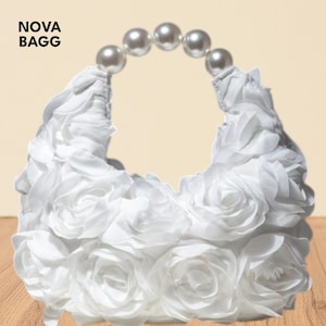 Puede incluir: Bolso de mano blanco con diseño floral y asa de perlas. El bolso está cubierto de rosas de tela blanca. El asa está hecha de perlas blancas grandes y redondas. El texto "NOVA BAGG" está en la esquina superior izquierda.