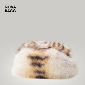 Puede incluir: Un bolso ovalado y esponjoso con una mezcla de pieles crema, marrón y beige. El bolso tiene un aspecto suave y texturizado. El texto "NOVA BAGG" está en la esquina superior izquierda. Este bolso es un accesorio elegante.