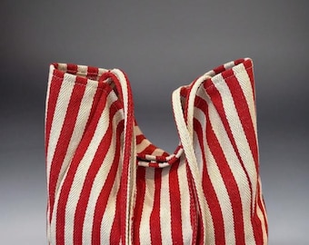 May include: A tote bag made of woven fabric featuring a bold pattern of vertical red and off-white stripes. The bag has two long, matching striped shoulder straps attached to the top edge, with a soft, unstructured shape and a rectangular base.