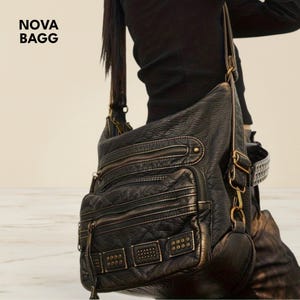 Peut inclure: Sac à bandoulière en cuir noir avec plusieurs compartiments zippés et des clous décoratifs en métal. Le sac a une longue bandoulière réglable. Le texte "NOVA BAGG" est visible en haut à gauche.