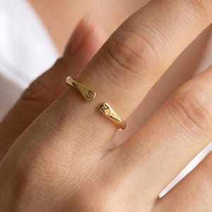 May include: A gold-toned open ring featuring a polished finish and two tapered ends. Each end is engraved with a single letter, specifically the characters S and Z, positioned to face each other across the open gap of the band on the finger.