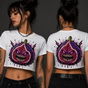 May include: White crop top featuring a graphic of a fig with a menacing face, fangs, and dripping details. The fig is purple and red, with pink lightning bolts. The shirt is worn by a person.