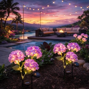 Könnte beinhalten: Gartenlandschaft mit solarbetriebenen Hortensienlichtern. Die lila und rosa Blütenlichter sind beleuchtet, vor dem Hintergrund eines Pools, einer Sitzecke und Lichterketten. Der Himmel zeigt eine Mischung aus Orange, Rosa und Lila.
