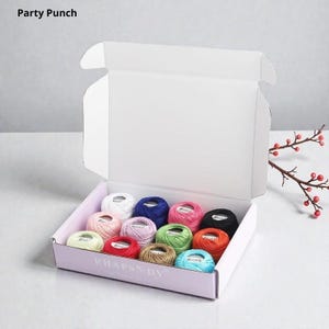 May include: A white cardboard box labeled Party Punch and RHAPSDY containing twelve small round spools of embroidery thread in various colors including white, blue, pink, green, red, black, orange, and light brown, arranged in three rows.