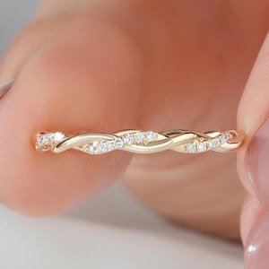 May include: A gold ring featuring a twisted band design with small, clear, sparkling stones embedded along the surface. The metal has a polished finish, and the structure consists of two intertwined strands that create a continuous, delicate pattern.