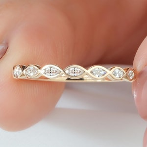 May include: A gold band ring featuring a series of marquise-shaped settings, each containing a small round white gemstone. The metal has a polished finish, and the stones are arranged in a continuous row along the top half of the band.