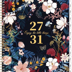 May include: A spiral-bound planner with a dark navy background featuring a colorful floral pattern of white, pink, and red flowers with green and blue foliage. The cover displays the gold text 27, Enjoy the little things, and 31, with monthly tabs.