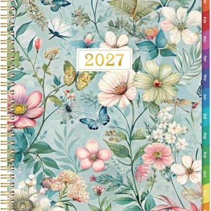 May include: A 2027 spiral-bound planner featuring a light blue cover with a botanical pattern of various flowers, green leaves, and butterflies. The center displays a white rectangular label with the gold text 2027. Colored monthly tabs are visible.