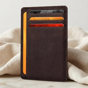 May include: A dark brown leather card holder featuring three horizontal slots on the front and one vertical side slot. The card holder contains a black card, a yellow card, a red card, and a solid yellow card visible in the side compartment.