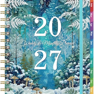 May include: A 2027 weekly and monthly planner with a spiral binding and a light blue elastic closure. The cover features a winter forest illustration with snow-covered trees, ferns, and mushrooms in shades of blue, teal, and white.