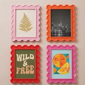 May include: Four rectangular picture frames with wavy, scalloped edges in pink, orange, red, and magenta. The frames contain a gold fern print, a black and white city skyline, a green print with the text WILD & FREE, and a colorful citrus fruit graphic.