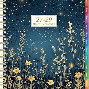 May include: A spiral-bound monthly planner with a dark blue night sky background featuring gold stars and golden wildflowers. A white rectangular label in the center displays the text 27-29 MONTHLY PLANNER. The side includes colorful monthly tabs.