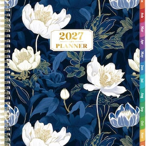 May include: A 2027 planner with a dark blue background featuring white and light blue floral patterns. The cover has a central rectangular label with the text 2027 PLANNER in gold. It includes a gold spiral binding and multicolored monthly tabs.