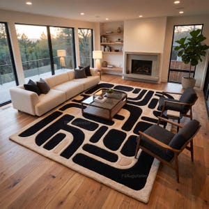 May include: A large rectangular area rug featuring a bold, high-contrast pattern of thick black geometric shapes set against a cream-colored background. The design consists of interconnected, rounded lines and solid blocks, creating a textured appearance on the floor.