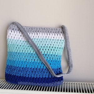 May include: A crocheted tote bag with a gray strap. The bag is made with a gradient of blue, green, and white yarn.