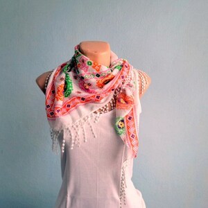 K&ouml;nnte beinhalten: Ein wei&szlig;er Schal mit einem rosa, orange und gr&uuml;nen Blumenmuster. Der Schal hat einen Fransenrand und ist um ein wei&szlig;es Tanktop gebunden.
