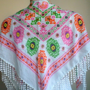 K&ouml;nnte beinhalten: Wei&szlig;er Baumwollschal mit einem farbenfrohen geometrischen Muster in den Farben Rosa, Orange, Gr&uuml;n und Lila. Der Schal hat einen Fransenrand.
