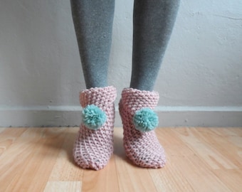 May include: A pair of pink knitted slipper socks with light blue pom poms on the top.