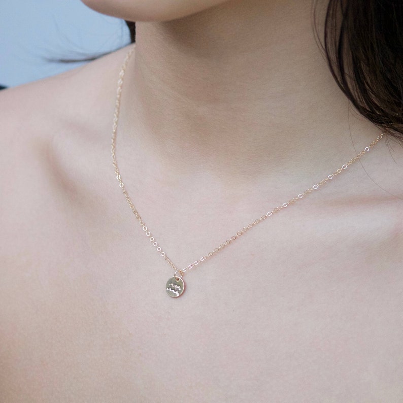 May include: A gold chain necklace with a small, round pendant featuring the astrological symbol for Aquarius.