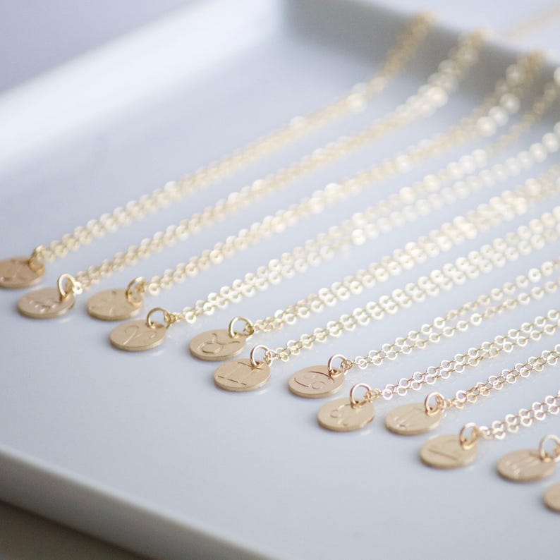 May include: A set of gold necklaces with small, round pendants featuring different zodiac signs. The necklaces are arranged in a row on a white surface.