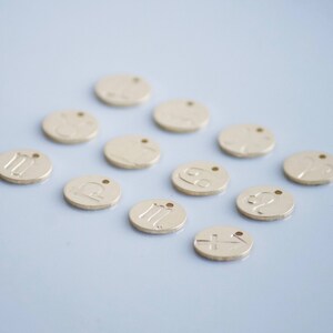 May include: Twelve gold-colored metal charms with different zodiac signs. The charms are round and have a hole at the top for attaching to a necklace or bracelet.