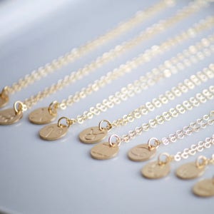 May include: A set of gold necklaces with zodiac symbols on the pendants. The necklaces are arranged in a row, with the pendants facing the viewer. The pendants are all different shapes and sizes, but they are all made of gold.