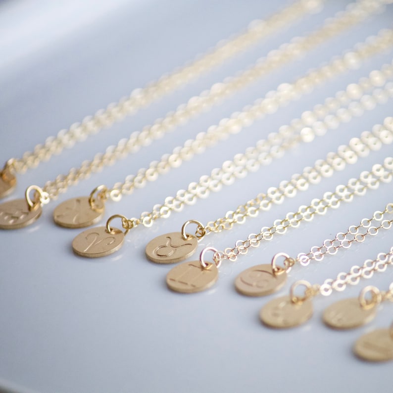 May include: A set of gold necklaces with zodiac symbols on the pendants. The necklaces are arranged in a row, with the pendants facing the viewer. The pendants are all different shapes and sizes, but they are all made of gold.