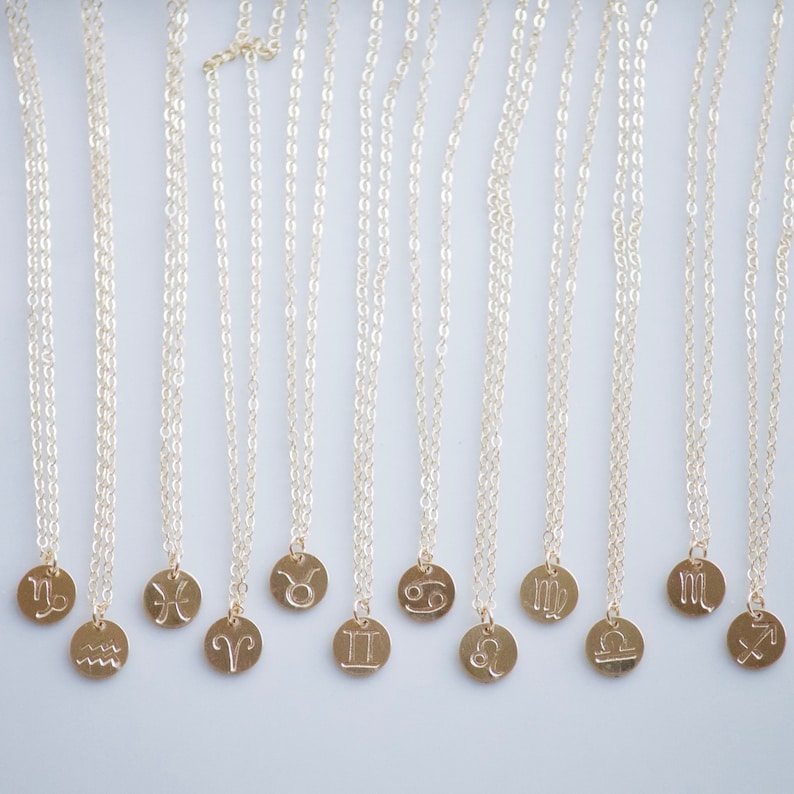 May include: A set of 12 gold necklaces with zodiac signs as pendants. The signs are: Capricorn, Aquarius, Pisces, Aries, Taurus, Gemini, Cancer, Leo, Virgo, Libra, Scorpio, and Sagittarius.