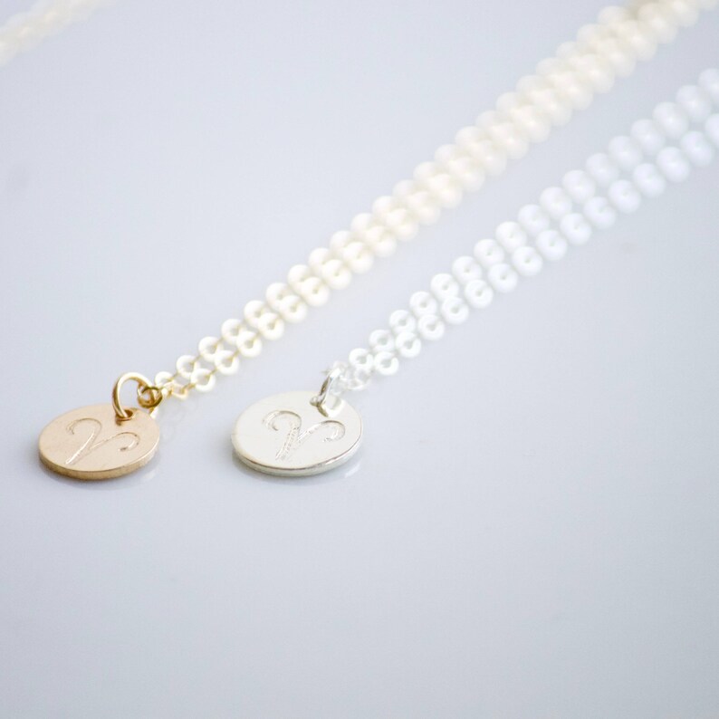 May include: Two delicate necklaces with a silver and gold pendant featuring the zodiac symbol for Aries. The necklaces are made of a fine chain.