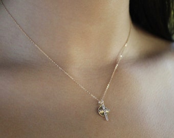 May include: A delicate gold chain necklace with a small cross pendant. The cross is made of gold and has a circular design with a smaller cross in the center.