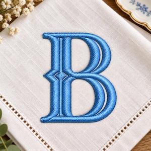 Può includere: Un tovagliolo di lino bianco con una lettera B maiuscola ricamata al centro in filo blu vibrante. La lettera ha un design audace e strutturato con un asse verticale e due anelli arrotondati. Il tovagliolo presenta un bordo con orlo a giorno.