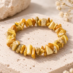 May include: A stretch bracelet composed of numerous irregular, tumbled stone chips in various shades of yellow, mustard, ochre, and cream. The stones have a smooth, polished finish and are strung together in a circular loop shape.