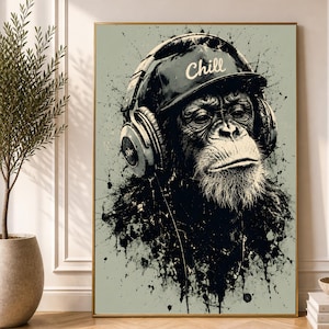 May include: A framed wall art print featuring a black and white illustration of a chimpanzee wearing large headphones and a baseball cap with the word Chill printed on the front. The artwork has a distressed ink splatter effect on a light background.