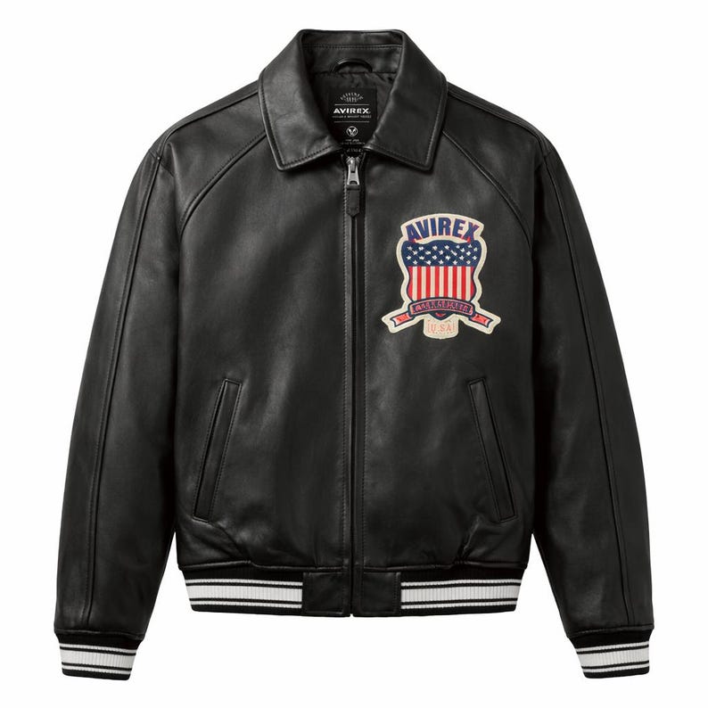 May include: Black leather jacket with a collared neckline and a zip-up front. Features a patch on the chest with a red, white, and blue design and the word "AVIREX". The jacket has white stripes on the cuffs and hem.