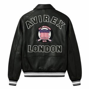 Peut inclure: Veste en cuir noire avec lettrage blanc et un écusson avec un bouclier et le texte "ALL AMERICANS 1975 LONDON". La veste a un col, des poignets côtelés et un ourlet rayé.