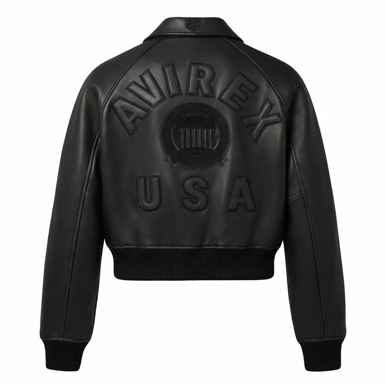 Puede incluir: Chaqueta bomber de cuero negro con el texto en relieve "AVIREX USA" en la espalda. La chaqueta tiene cuello, pu&ntilde;os y dobladillo de canal&eacute;. La parte trasera presenta un emblema circular con l&iacute;neas verticales.