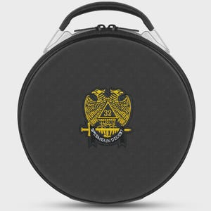 May include: A round black carrying case with a top handle and a zipper closure. Centered on the front is an embroidered patch featuring a yellow double-headed eagle, a triangle with the number 32, a horizontal sword, and the text SPES MEA IN DEO EST.