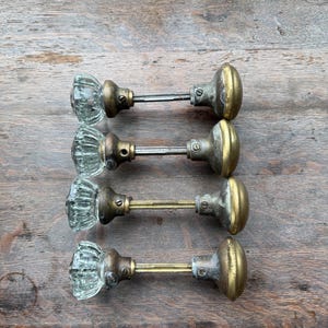 May include: Four antique glass and brass door knobs. The glass knobs have a ribbed design, and the brass components show signs of age. The knobs are connected by a metal rod. The background is a wooden surface.