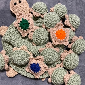 May include: A collection of crocheted turtle toys in various shades of green, beige, and brown. The turtles have different colored shell patterns, including green, orange, and blue.