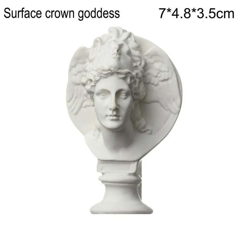 May include: A white bust of a goddess with a crown and wings, measuring 7 inches tall, 4.8 inches wide, and 3.5 inches deep. The sculpture has the text "Surface crown goddess" at the top.
